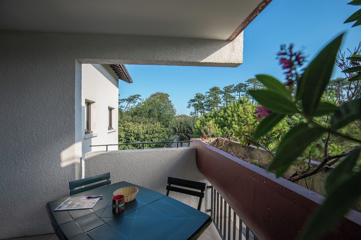 A balcony with a table and chairs, overlooking a garden and a building.