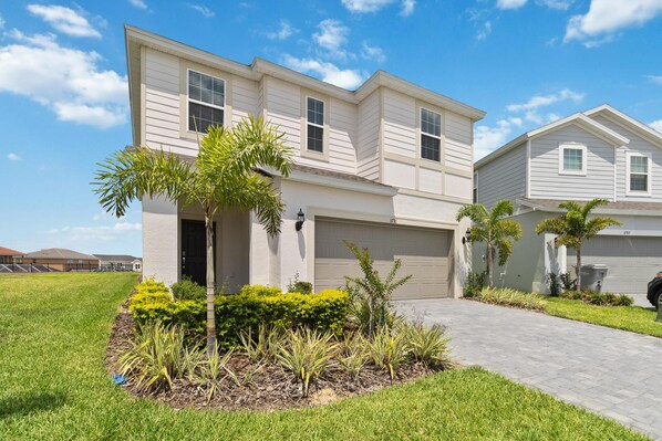A two-story residential house with a garage, a paved driveway, and a well-maintained lawn with various plants. - Amazing 7/5 Vacation Home at Windsor Island Resort!!! (Davenport)