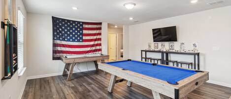 A room with a pool table, a billiards table, and an American flag.