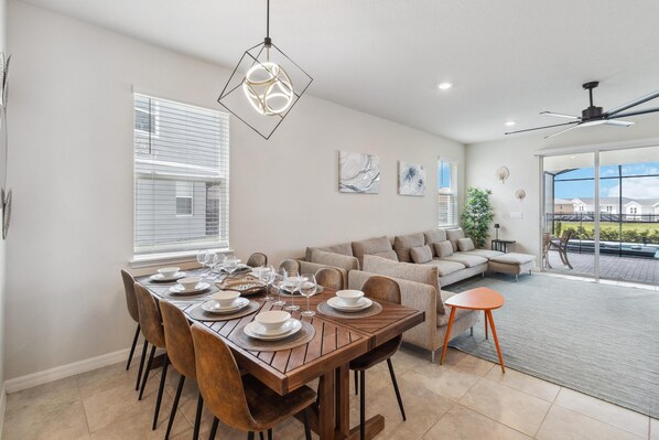 A dining area with a wooden table set for six, a sofa, and a balcony with a view. - Amazing 7/5 Vacation Home at Windsor Island Resort!!! (Davenport)