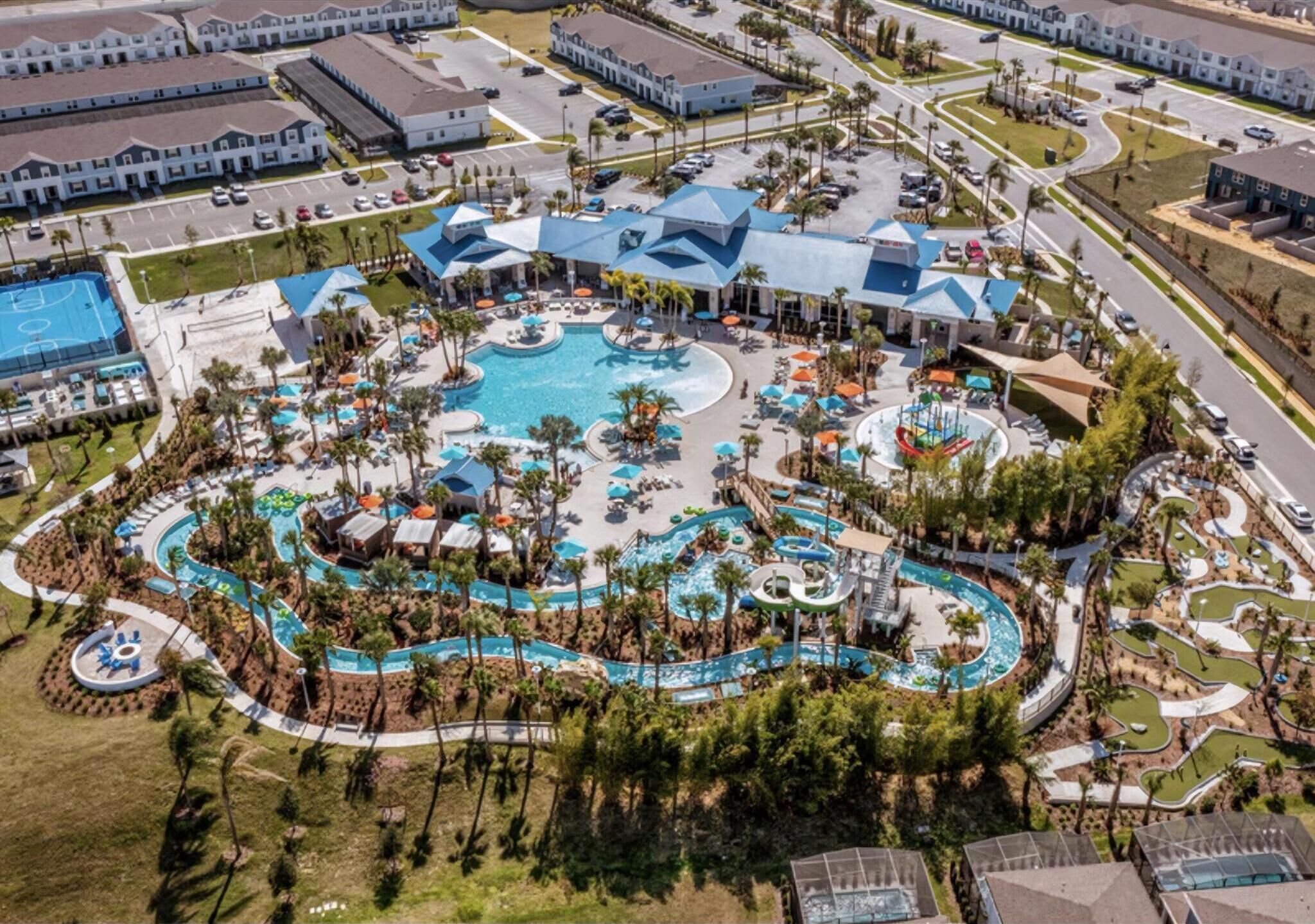 An aerial view of a resort with a central pool area, multiple buildings, and a parking lot.