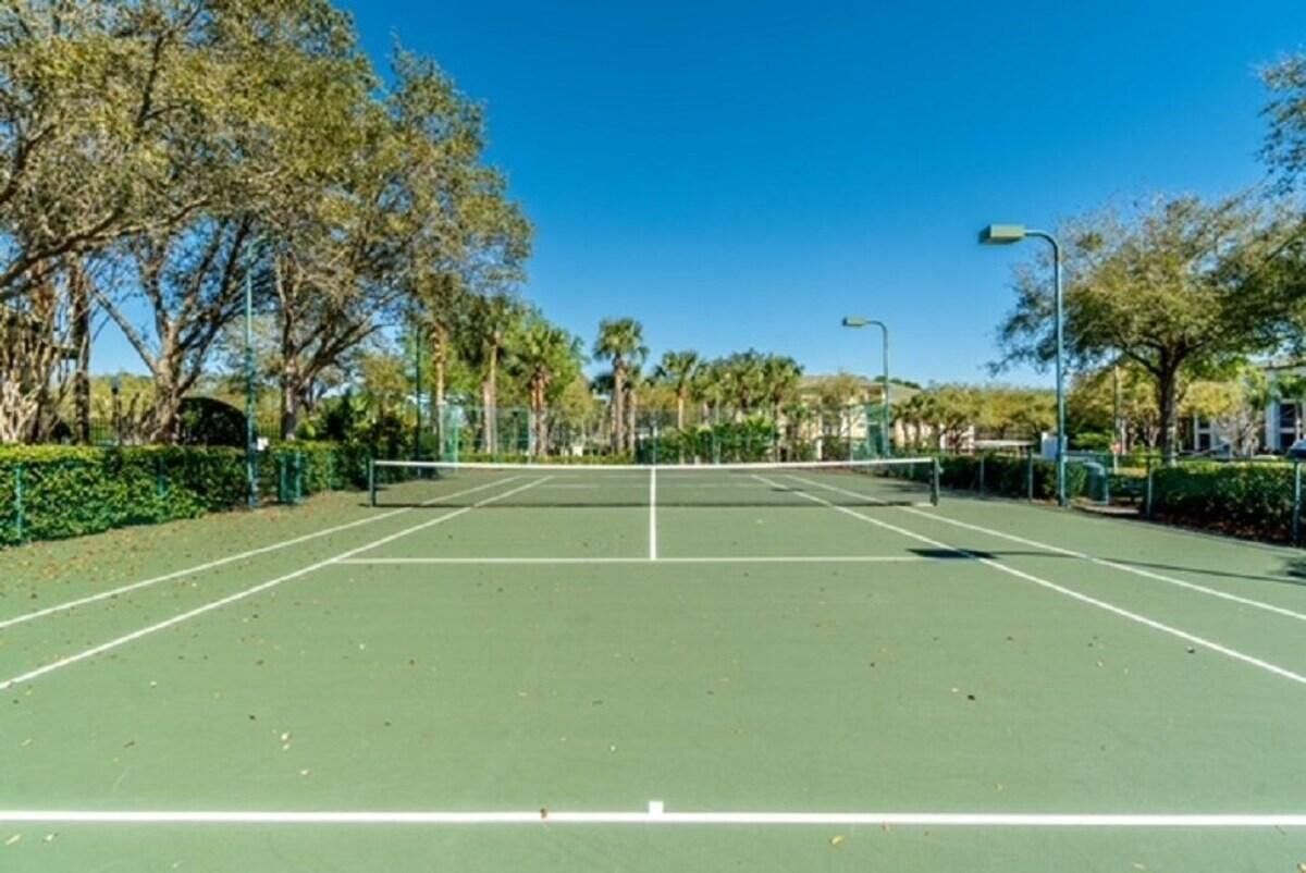 Cancha de tenis al aire libre con red, rodeada de árboles y cielo despejado.