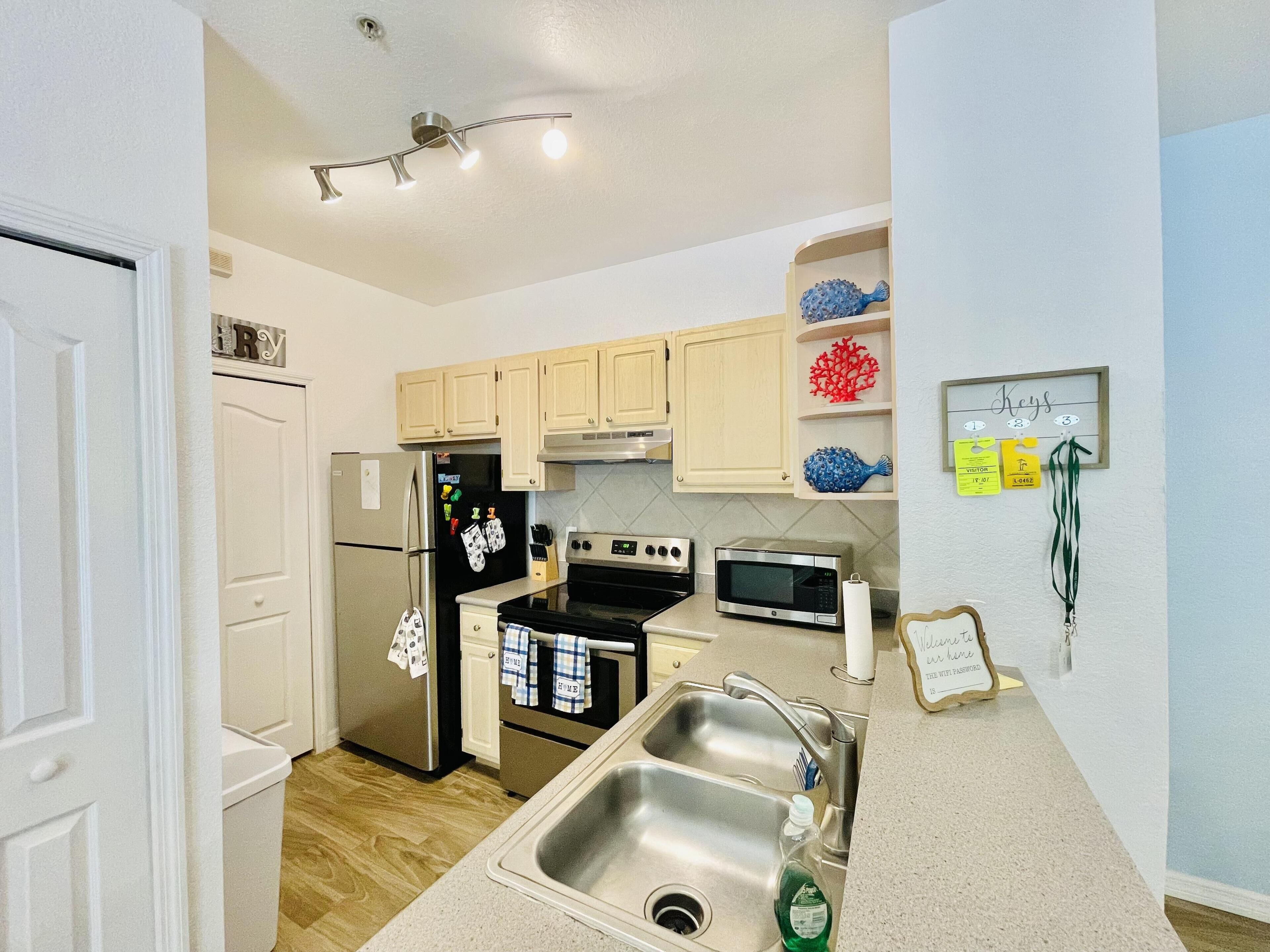 A modern kitchen with a stainless steel refrigerator, oven, microwave, and sink. There are wooden cabinets and a ceiling light fixture.