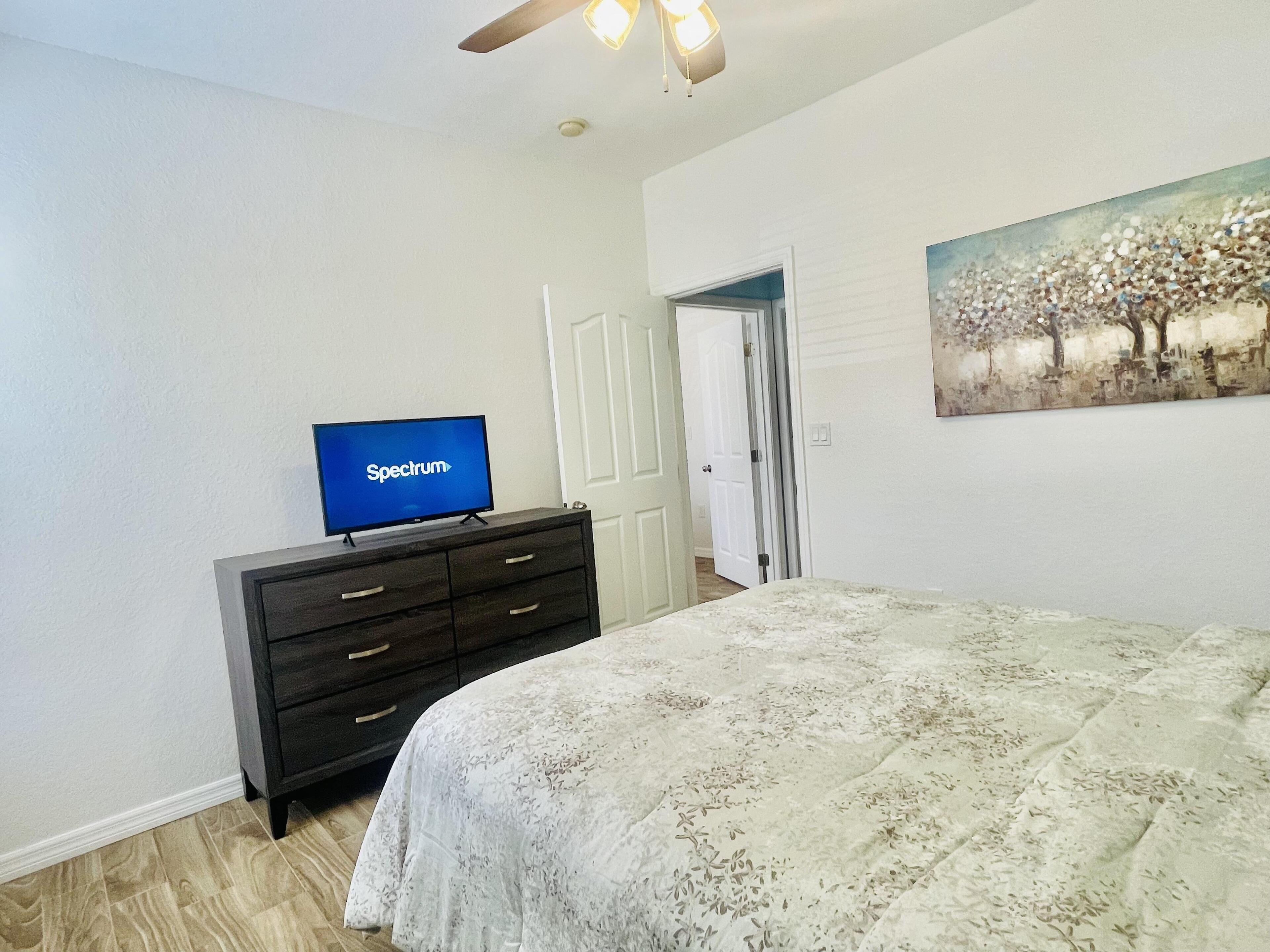 A bedroom with a bed, a dresser, a television displaying 'Spectrum', and a door leading to another room.