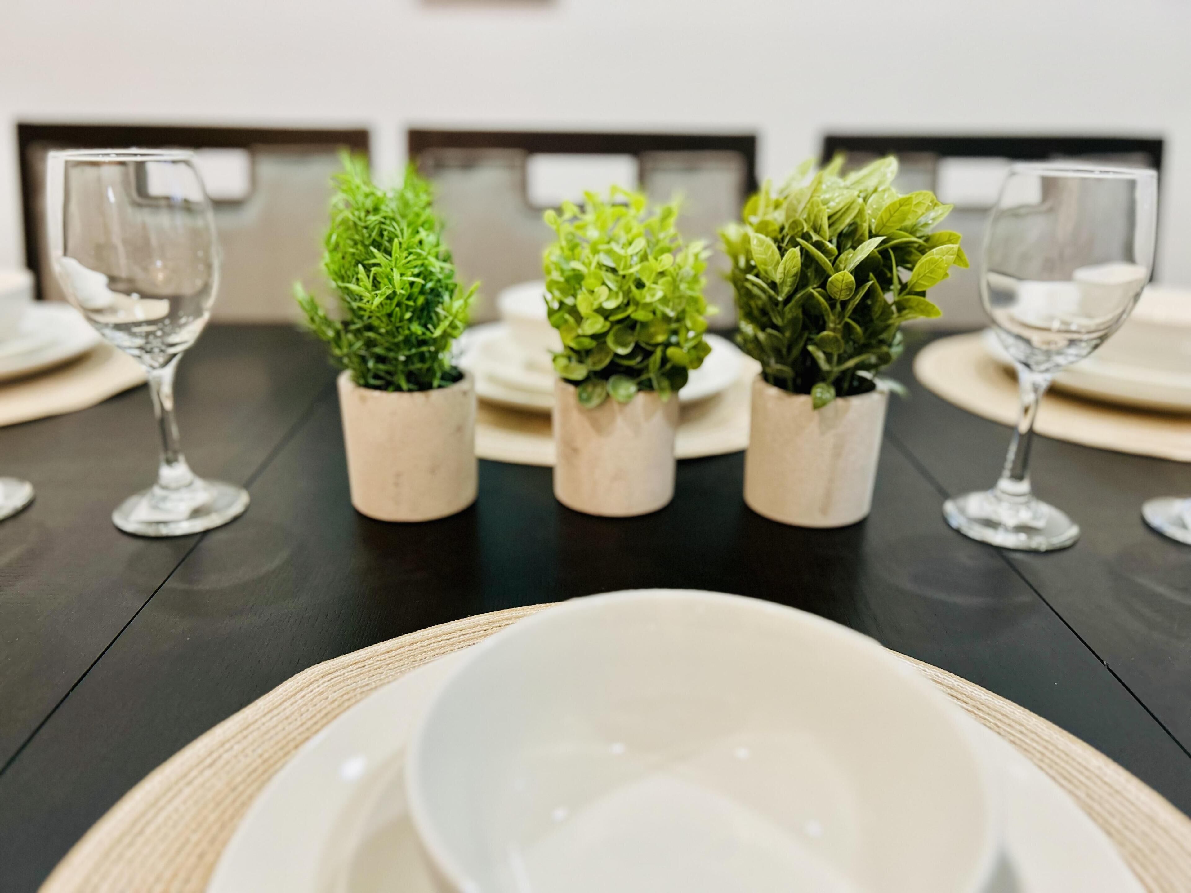 Une table à manger agrémentée de quatre petites plantes en pot et de deux verres à vin.