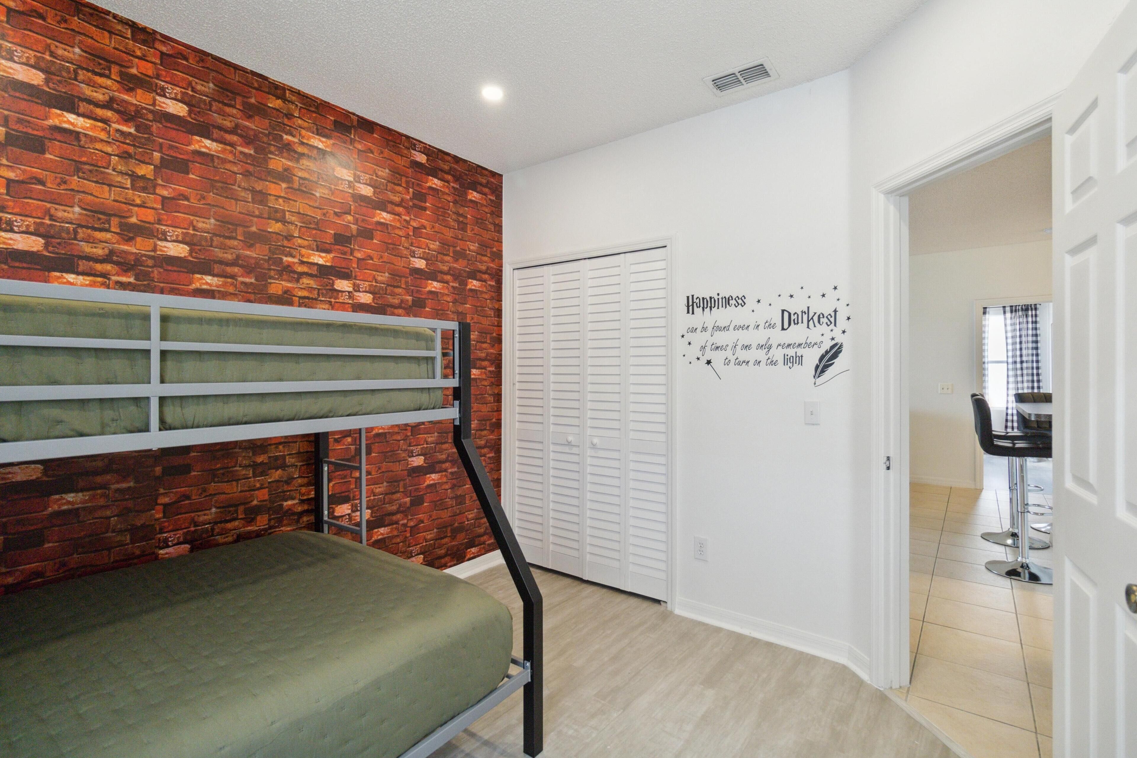 A room with a bunk bed, a brick wall, a white door, and a wall decal with a quote.