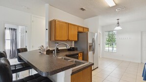 A modern kitchen with granite countertops, wooden cabinets, a stainless steel refrigerator, and a built-in dishwasher. - 5/3 Pool Home Located in Sunset Ridge Community! (Davenport)