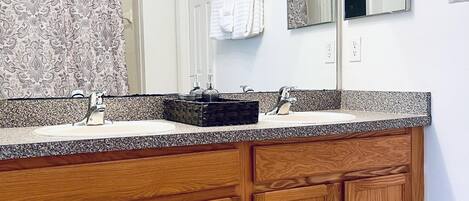 A bathroom with a double vanity, wooden cabinets, a large mirror, and a patterned shower curtain.