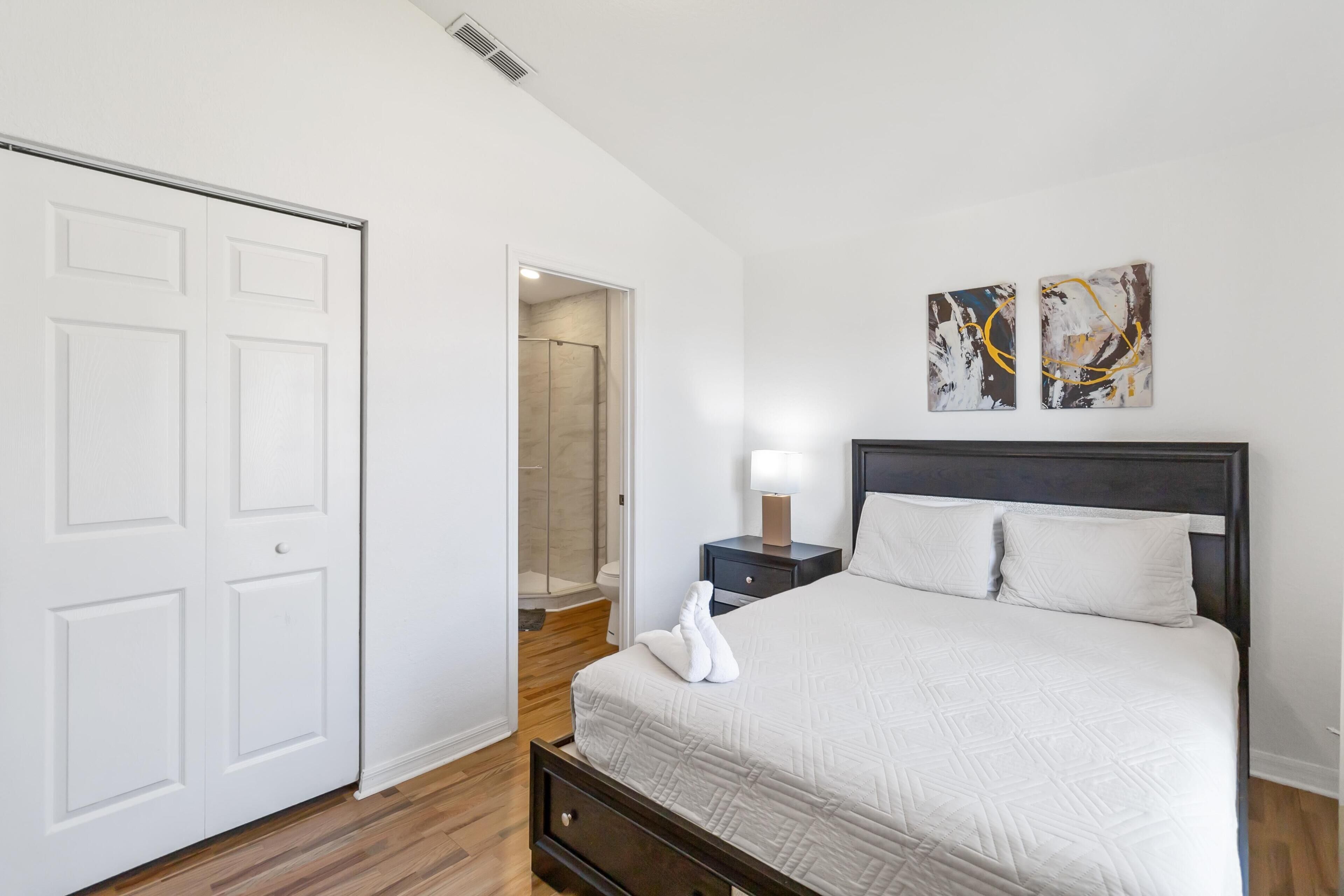 Un dormitorio con cama, mesita de noche, puerta y zona de ducha.
