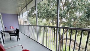 A balcony with a glass table and chairs, overlooking a grassy area with trees. - Huge Screened Patio That Overlooks Lake Buck, Near Famous Attractions!! (Kissimmee)