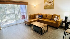 A living room with a brown leather sofa, a wooden coffee table, and a painting of flowers on the wall. - Huge Screened Patio That Overlooks Lake Buck, Near Famous Attractions!! (Kissimmee)