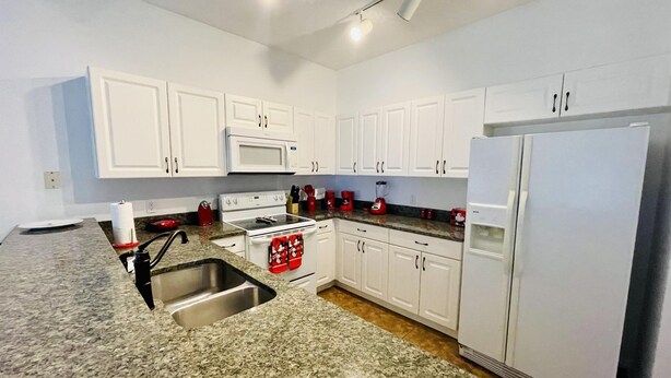 A modern kitchen with white cabinets, a granite countertop, stainless steel sink, and white appliances including a microwave, stove, and refrigerator. - Huge Screened Patio That Overlooks Lake Buck, Near Famous Attractions!! (Kissimmee)
