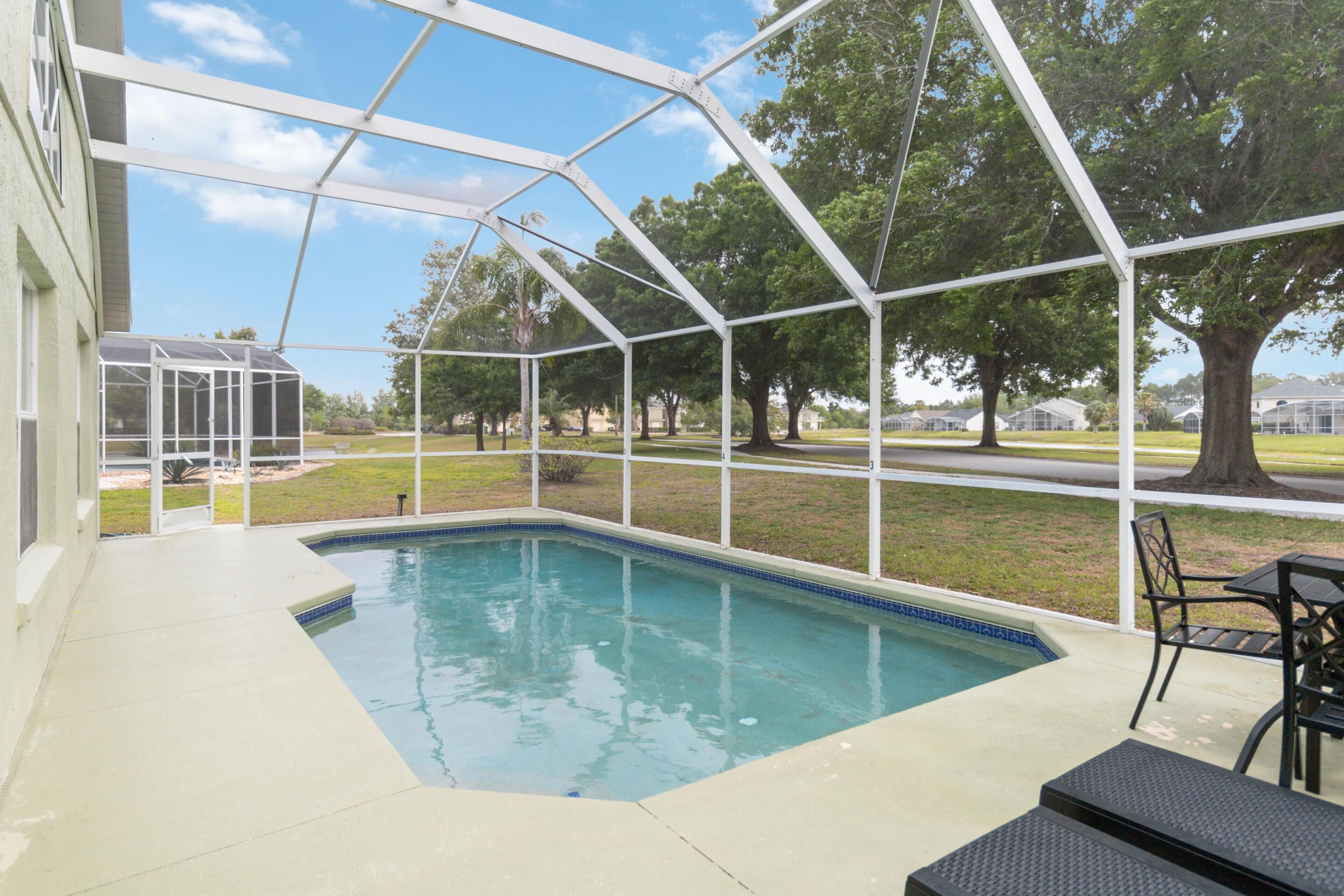 A covered outdoor swimming pool with a patio area, surrounded by trees and a clear sky.