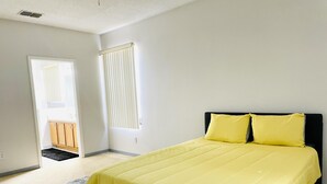 Une chambre à coucher avec un lit, une fenêtre avec des stores, une porte donnant sur une salle de bain et un petit tapis.