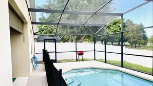 Une piscine extérieure couverte, avec un barbecue rouge et un tuyau d’arrosage.
