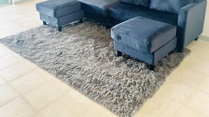Un salon avec un canapé d’angle bleu, un tapis à poils longs gris et une estampe botanique encadrée accrochée au mur.