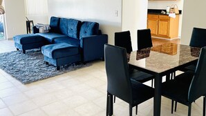 Un salon moderne avec un canapé bleu, une table à manger avec des chaises et un coin cuisine doté de meubles en bois.