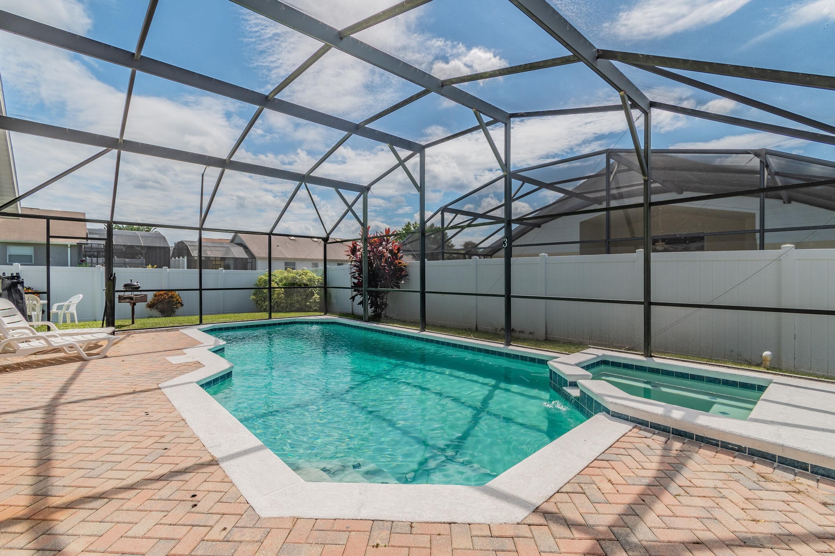 A covered swimming pool with a brick patio and lounge chairs.