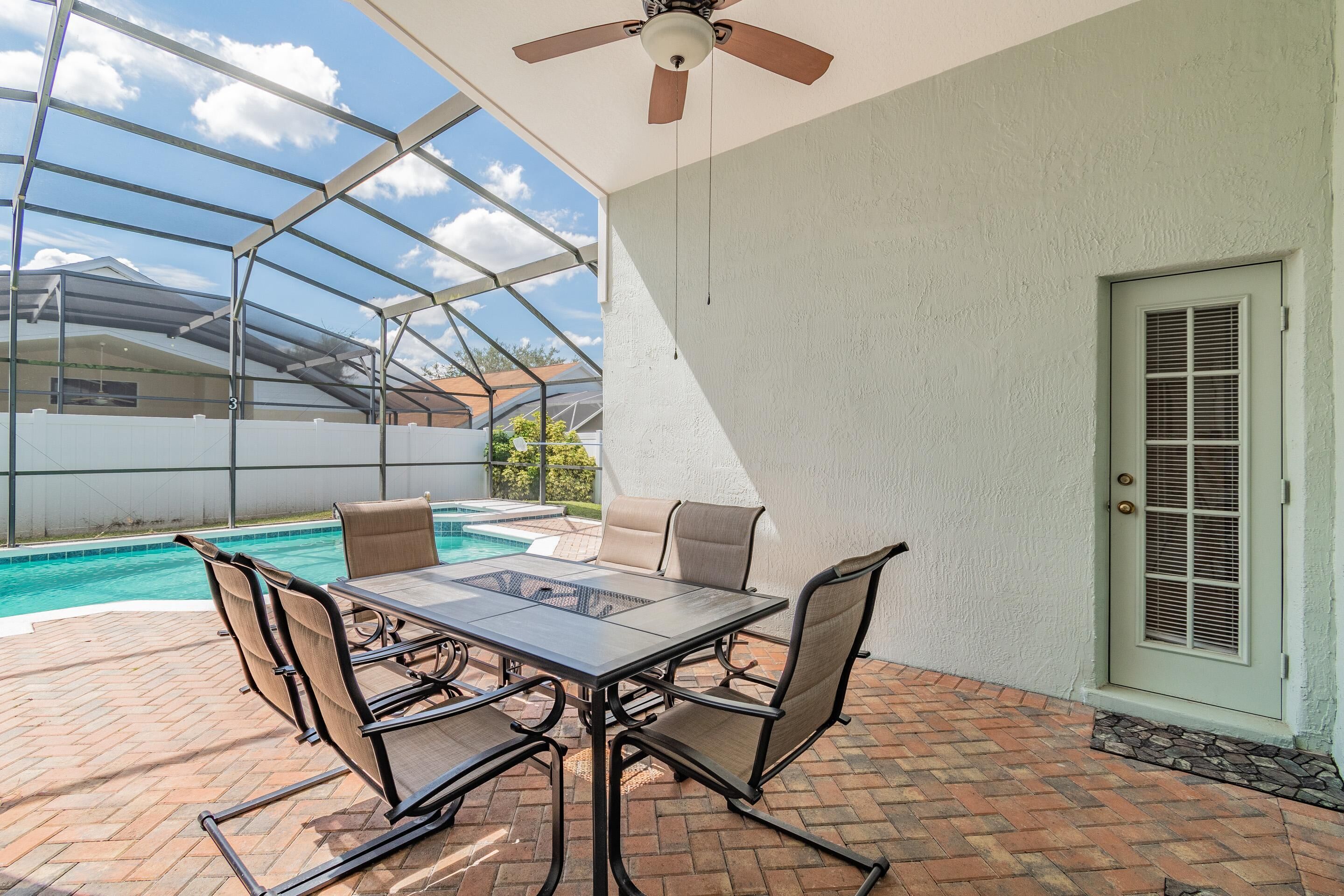 A covered patio with a glass ceiling, a pool, and a dining area with chairs and a table.