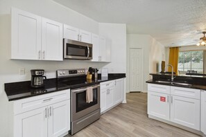A modern kitchen with white cabinets, stainless steel appliances, and a black countertop. - 5/4 Pool Home Located in Sunset Ridge Community! (Davenport)