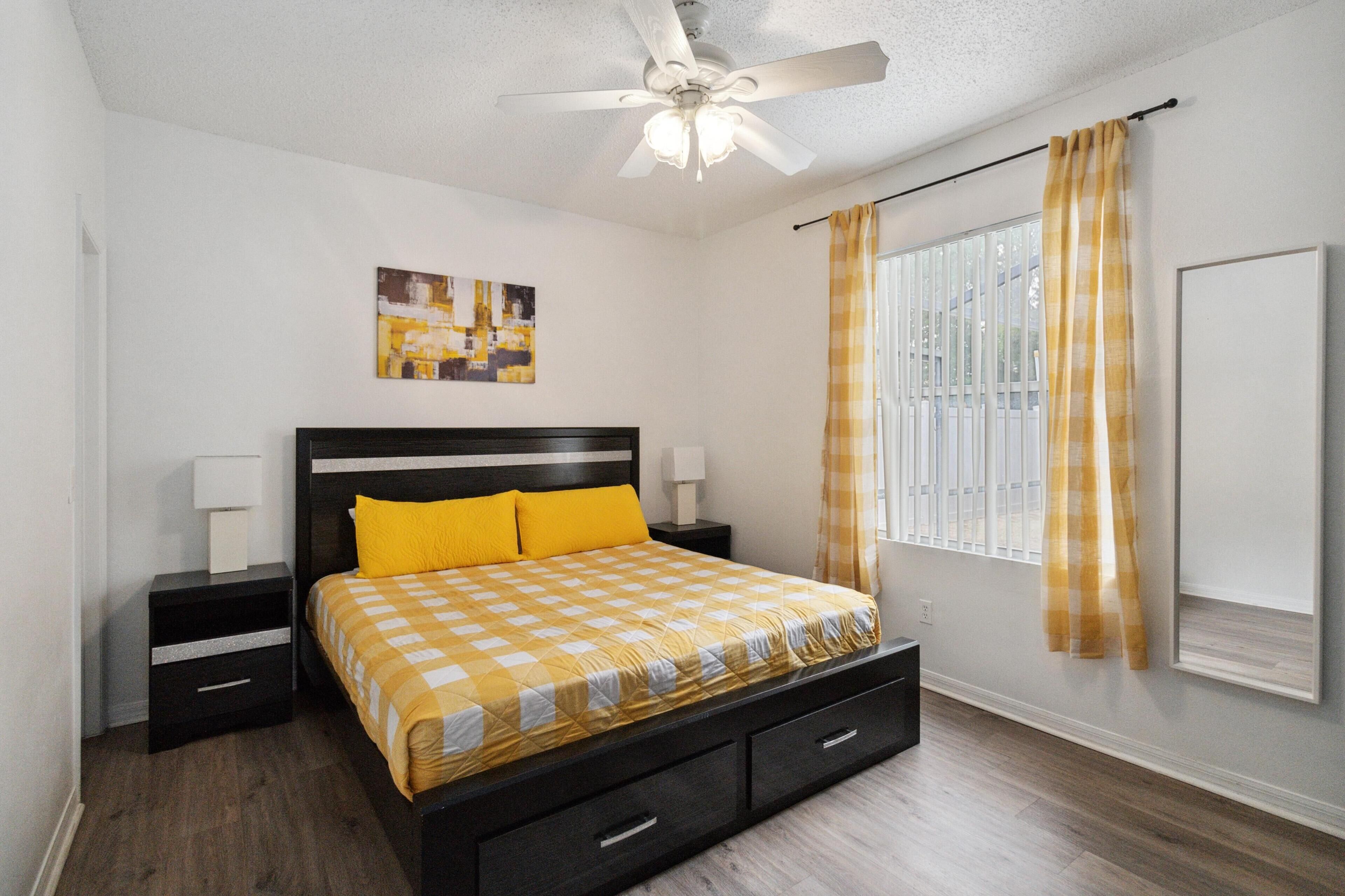 A bedroom with a bed, nightstands, a ceiling fan, and a window with curtains.
