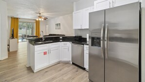 A modern kitchen with white cabinets, a stainless steel refrigerator, and a black countertop. - 5/4 Pool Home Located in Sunset Ridge Community! (Davenport)