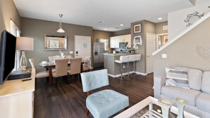 A modern living room with a sofa, a dining area with a table and chairs, a kitchen with a bar, and a staircase. - 4/3 Townhouse Near Disney!! (Kissimmee)