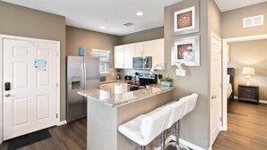 A modern kitchen with granite countertops, stainless steel appliances, and a central island with bar stools. - 4/3 Townhouse Near Disney!! (Kissimmee)