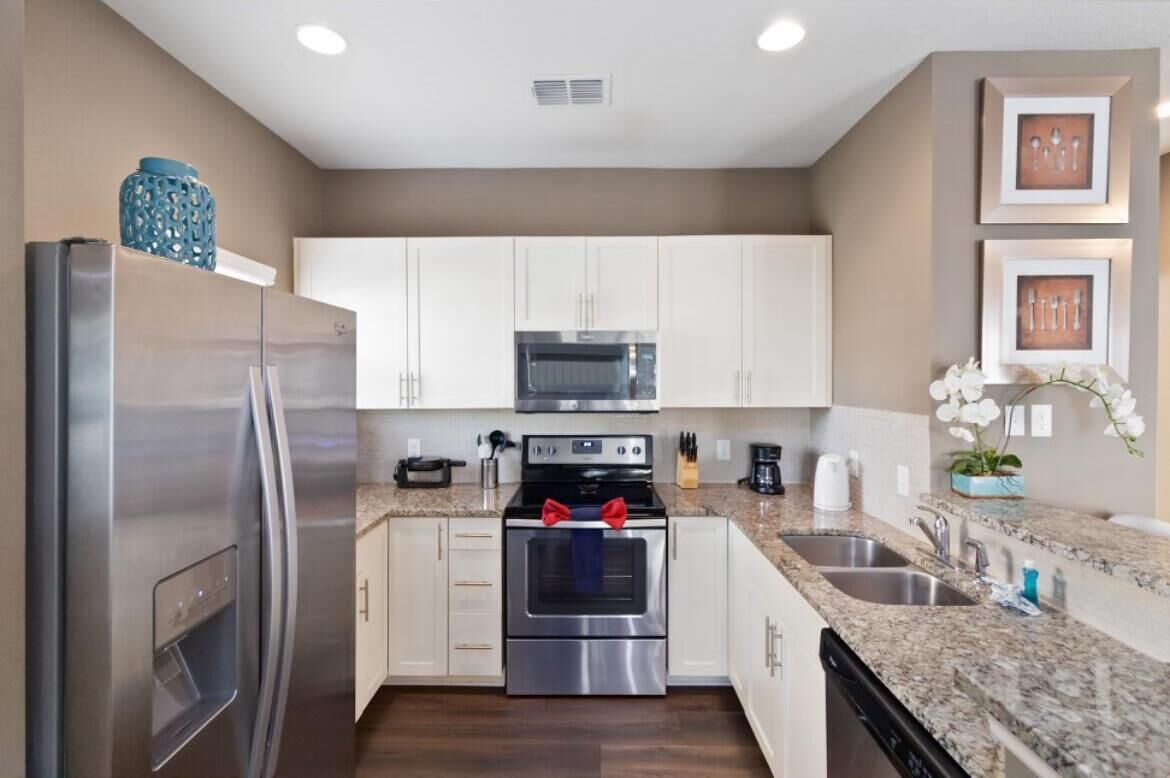 A modern kitchen with stainless steel appliances, white cabinets, granite countertops, and decorative elements like a blue vase and framed pictures.