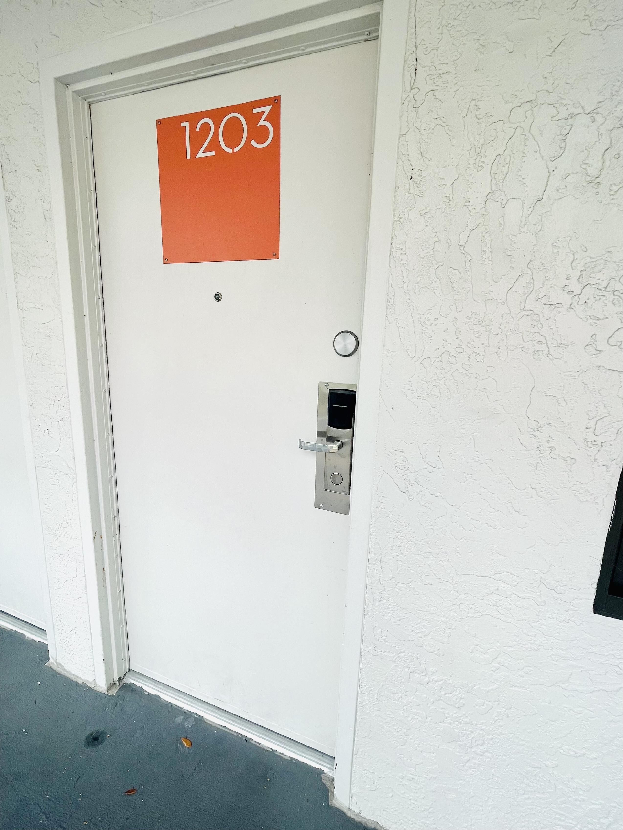 A white door with a number plate reading "1203" and a doorbell.