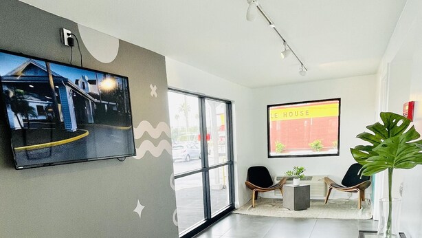 A modern hotel lobby with a large TV screen, comfortable seating, and a large window.