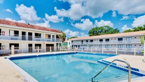 A hotel with a swimming pool, multiple balconies, and a clear blue sky.