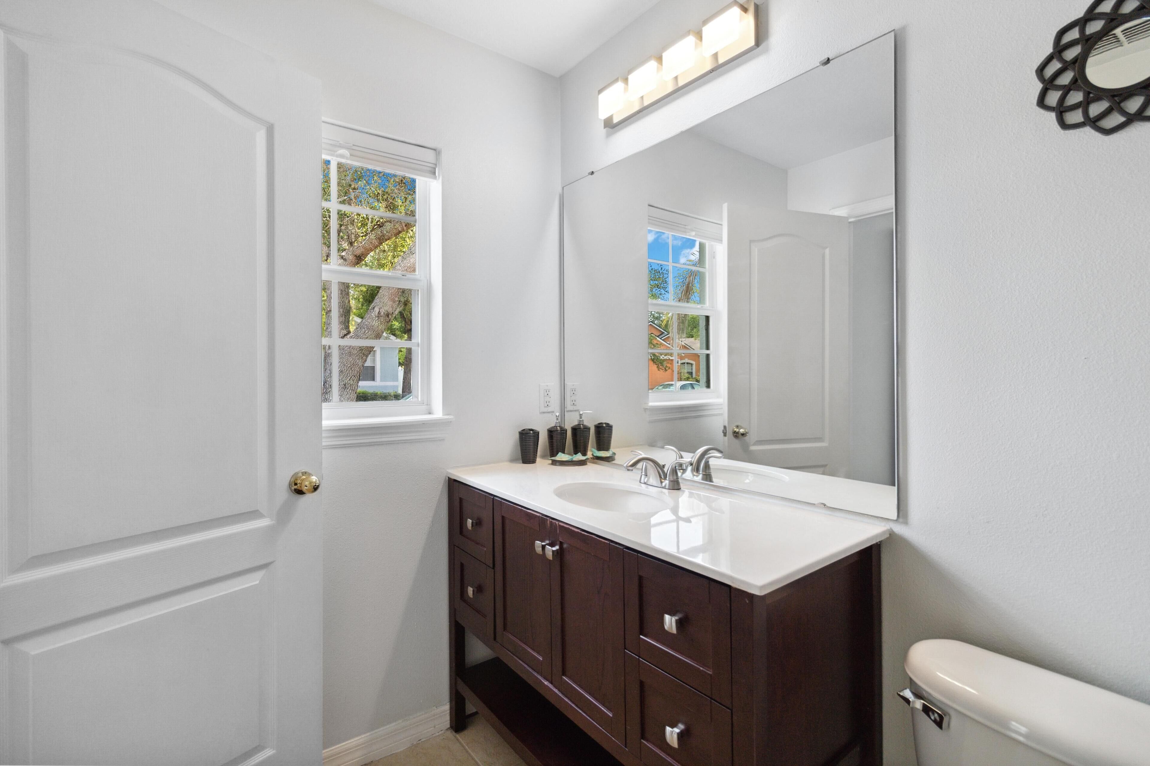 A bathroom with a white vanity, a large mirror, and a window.