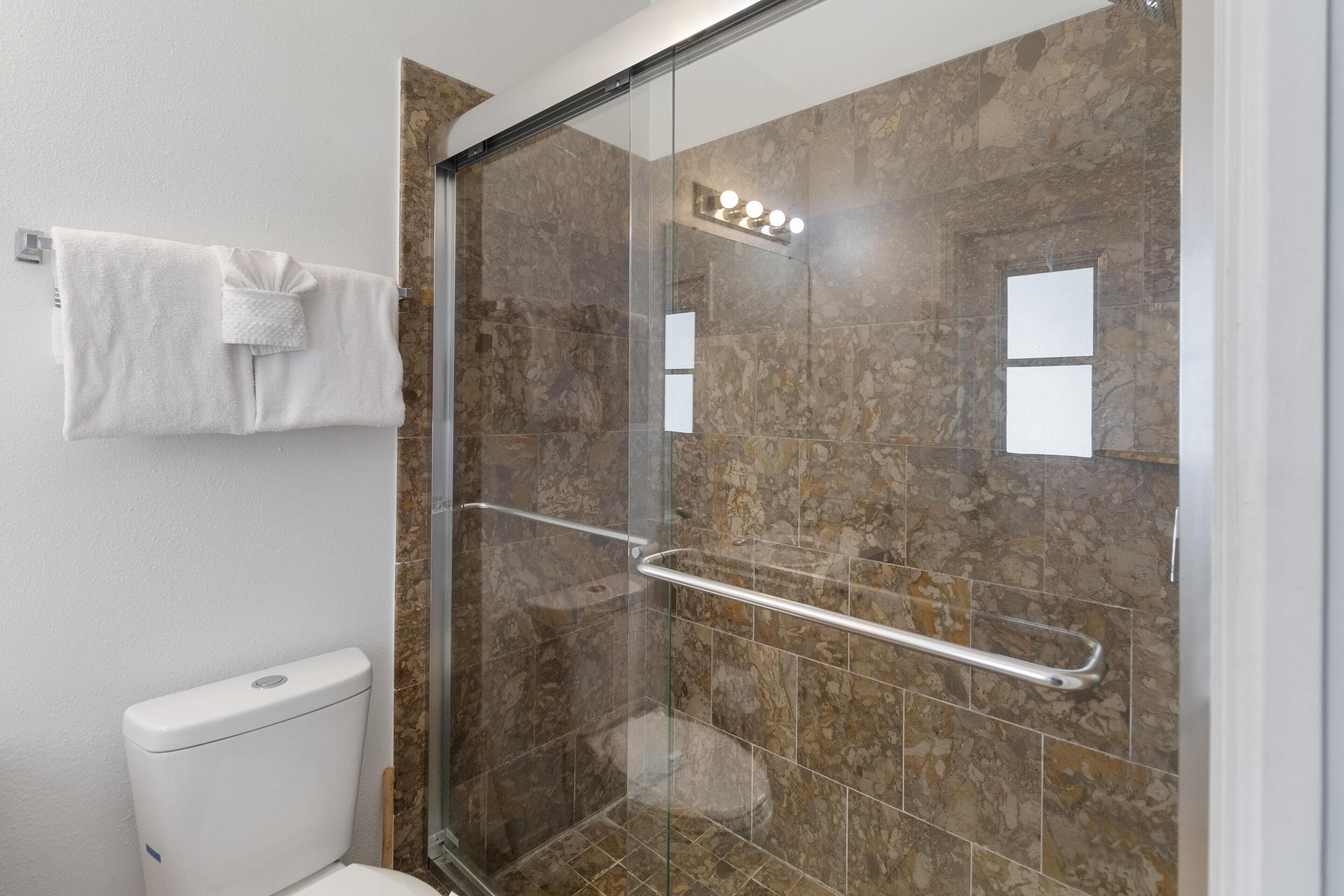 A modern bathroom with a glass-enclosed shower, marble tiles, a white toilet, and a towel rack.