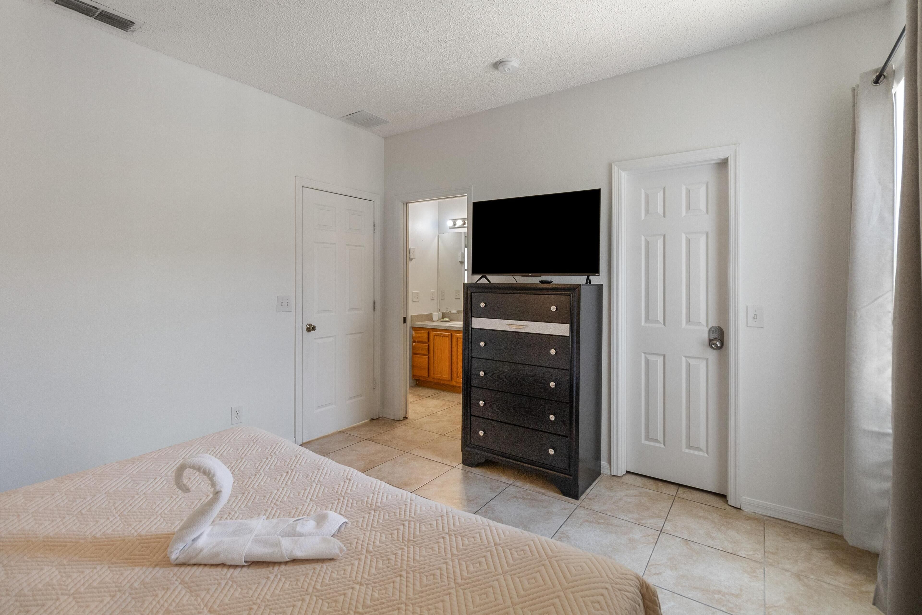 Une chambre à coucher comprenant un lit, une commode, un téléviseur et une porte donnant sur une salle de bain.