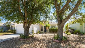 A residential property with a gravel driveway, mature trees, and a white garage door. - 5/3 Pool Home Located in Sunset Ridge Community! (Davenport)
