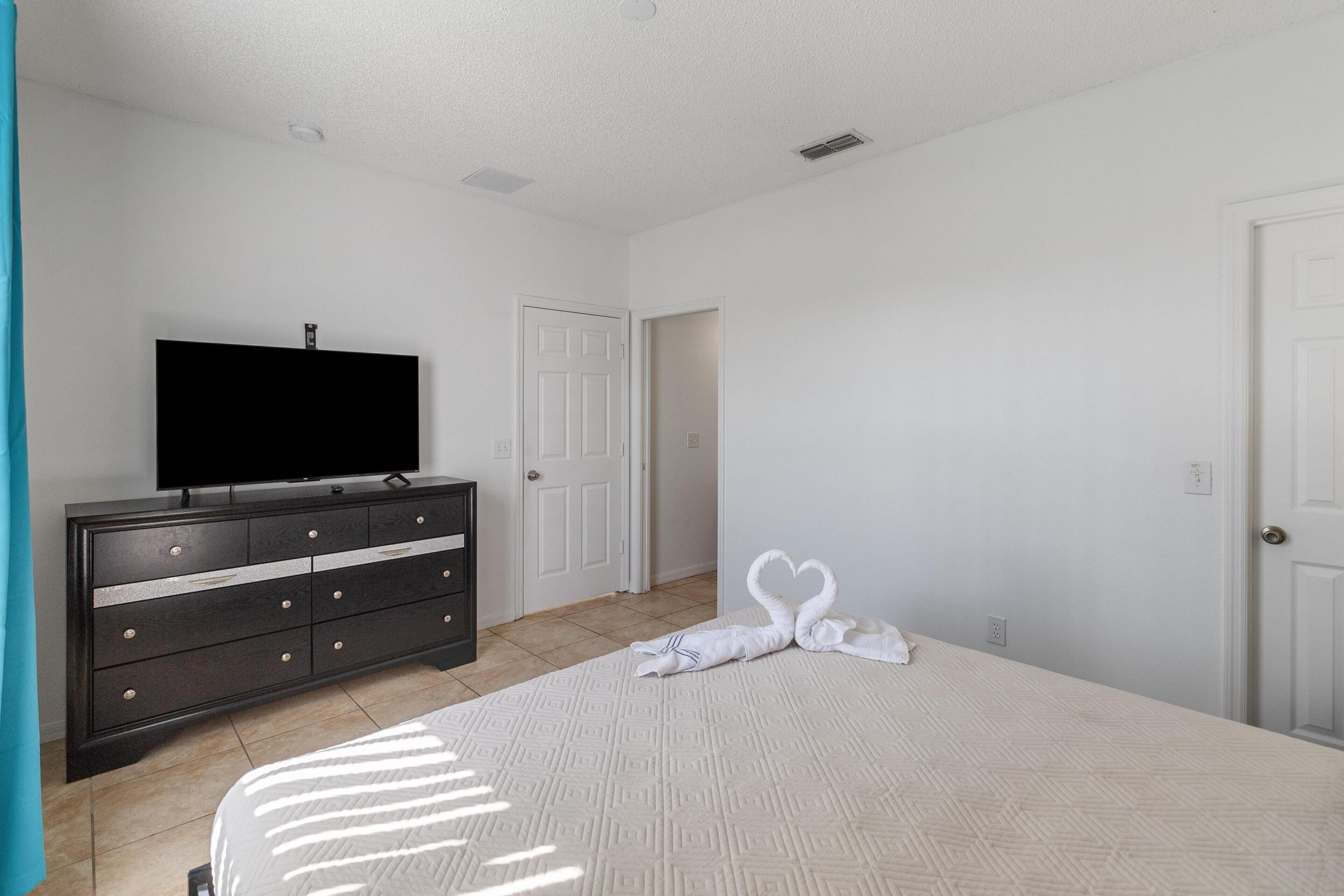 A bedroom with a bed, a dresser, a television, and two white doors.