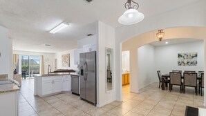 A spacious kitchen with white cabinets, a stainless steel refrigerator, and a dining area with a table and chairs. - 5/3 Pool Home Located in Sunset Ridge Community! (Davenport)