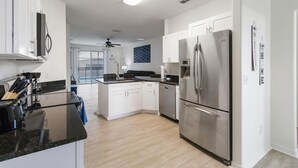 A modern kitchen with white cabinets, a stainless steel refrigerator, and a black countertop.