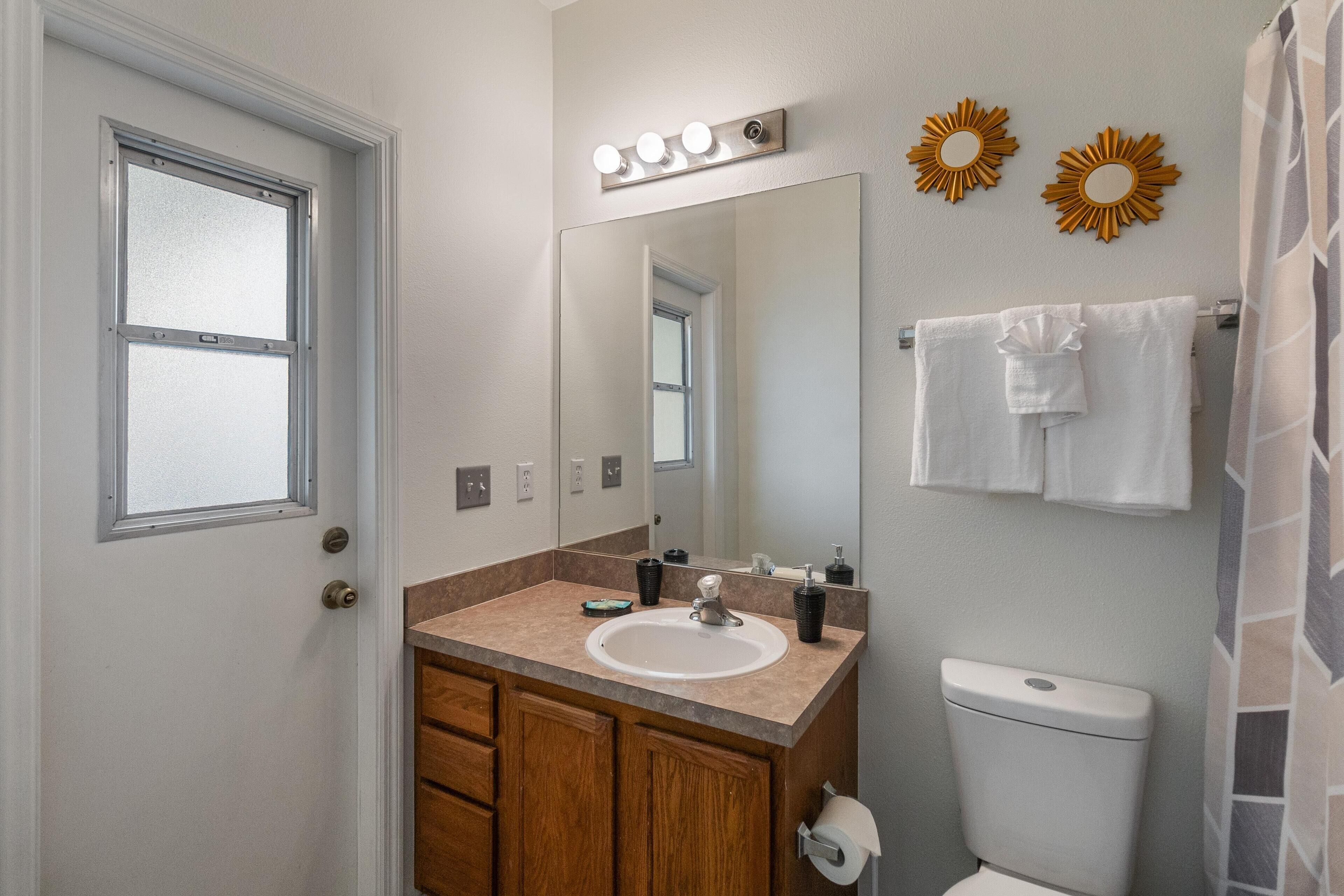 A bathroom with a white sink, wooden cabinets, a mirror with lights, and a toilet.