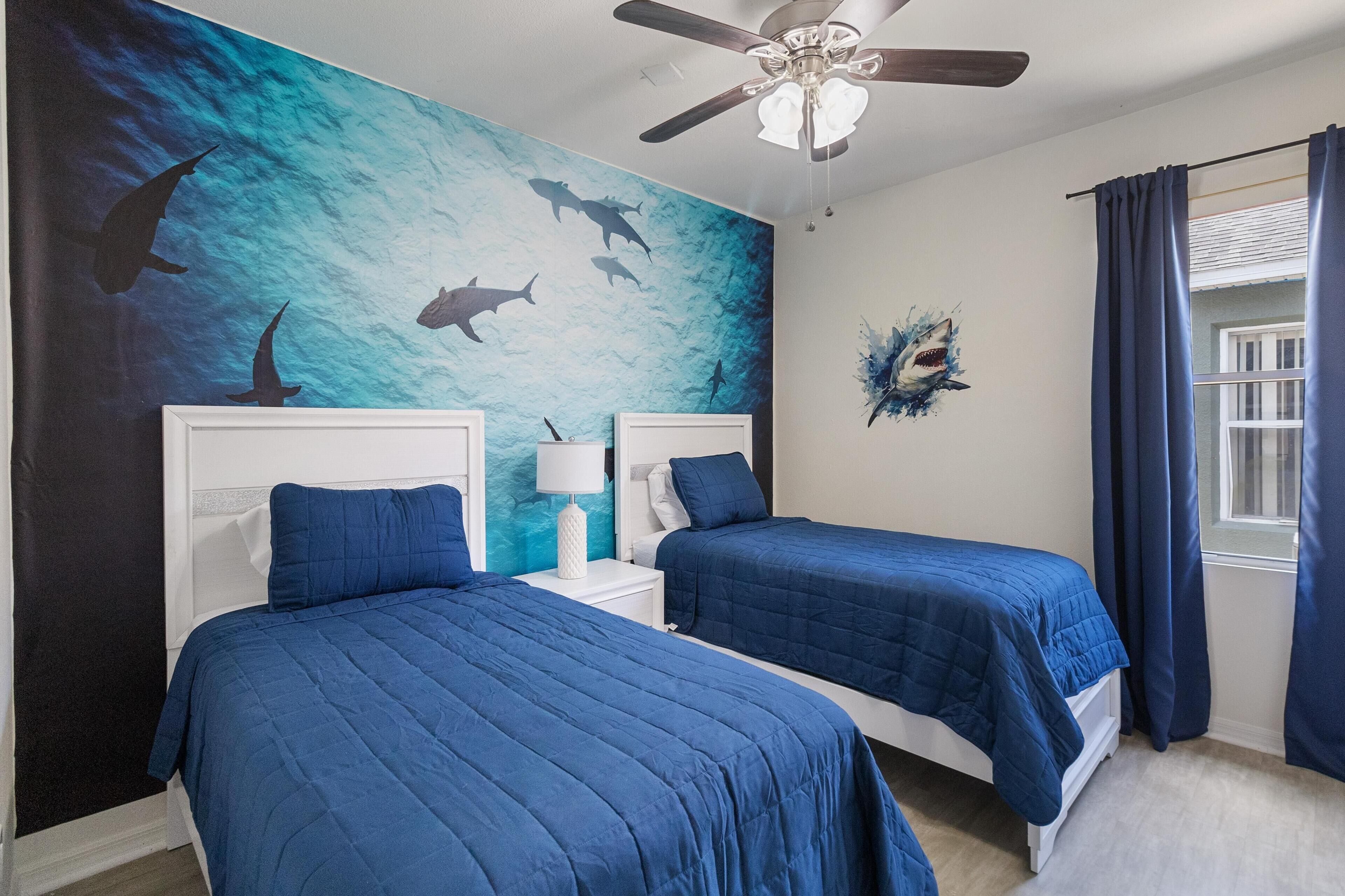 Une chambre avec deux lits, un ventilateur de plafond et une fresque représentant des requins sur le mur.