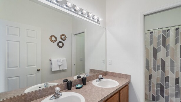A bathroom with two sinks, a large mirror, and a shower with a geometric tile pattern.