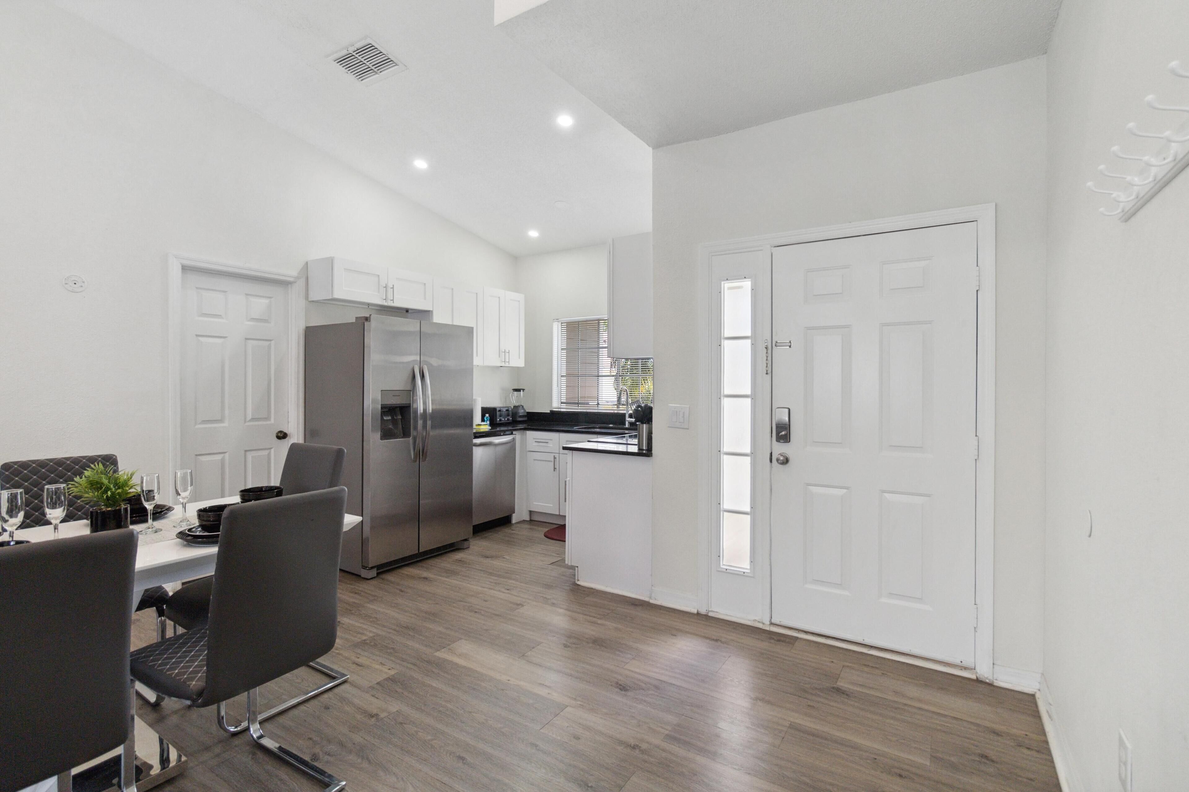 A modern kitchen with white cabinetry, stainless steel appliances, and a dining area with a table and chairs.