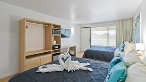 Ein Hotelzimmer mit zwei Betten, einem Fernseher, einem Holzschrank und einem Balkon mit Blick.