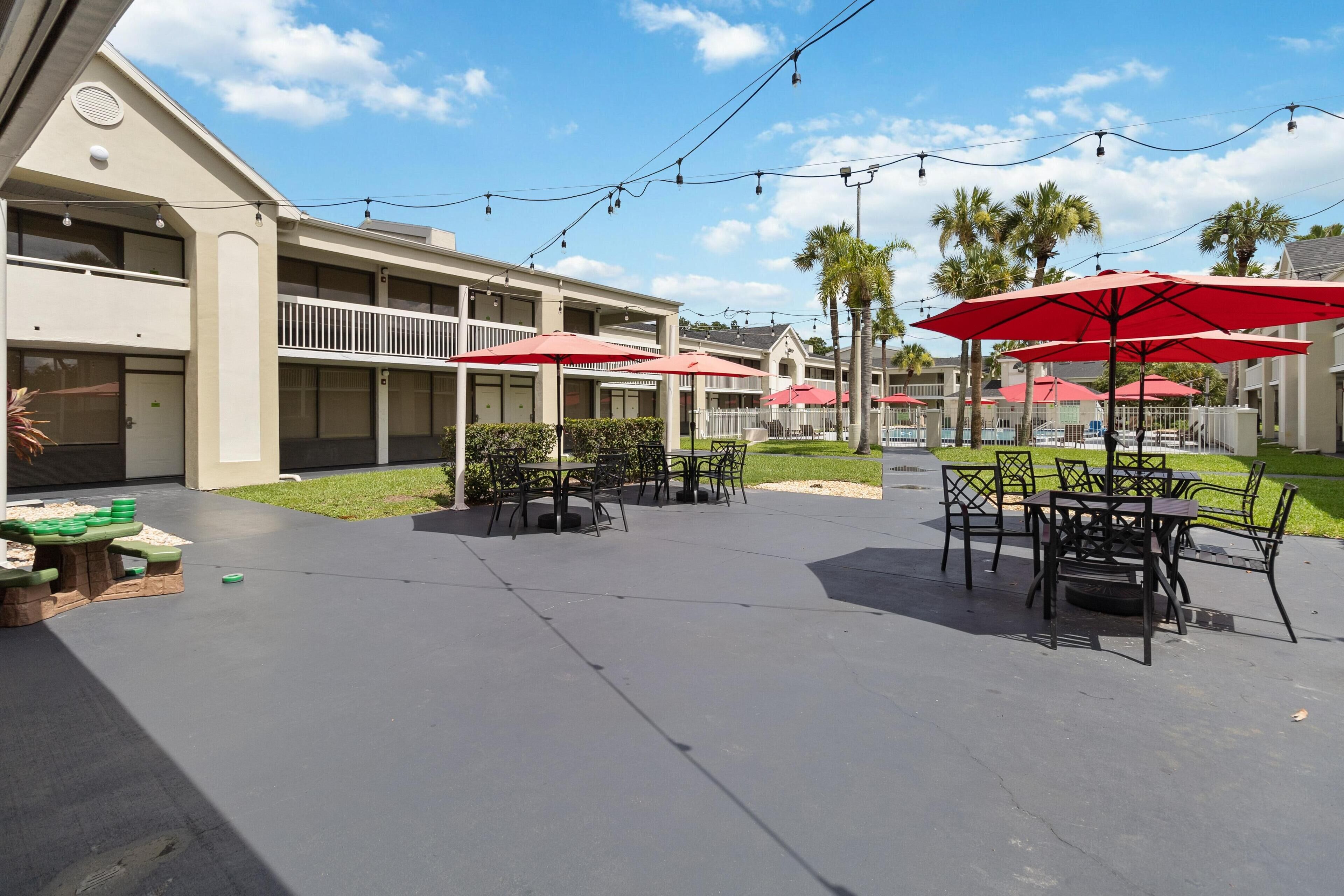 A hotel courtyard with outdoor seating, palm trees, and string lights.