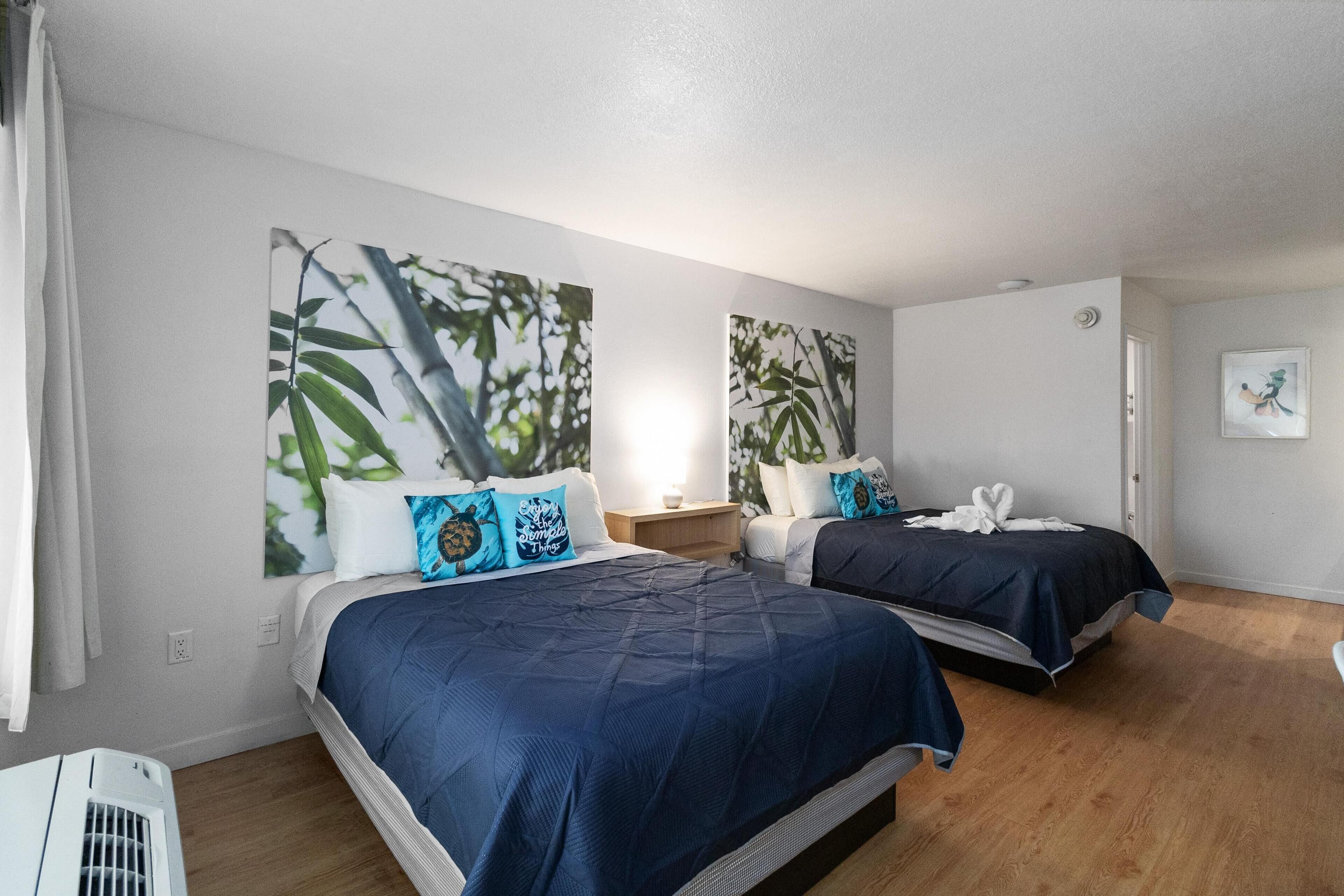Habitación de hotel con dos camas, una mesita de noche y aire acondicionado de pared.