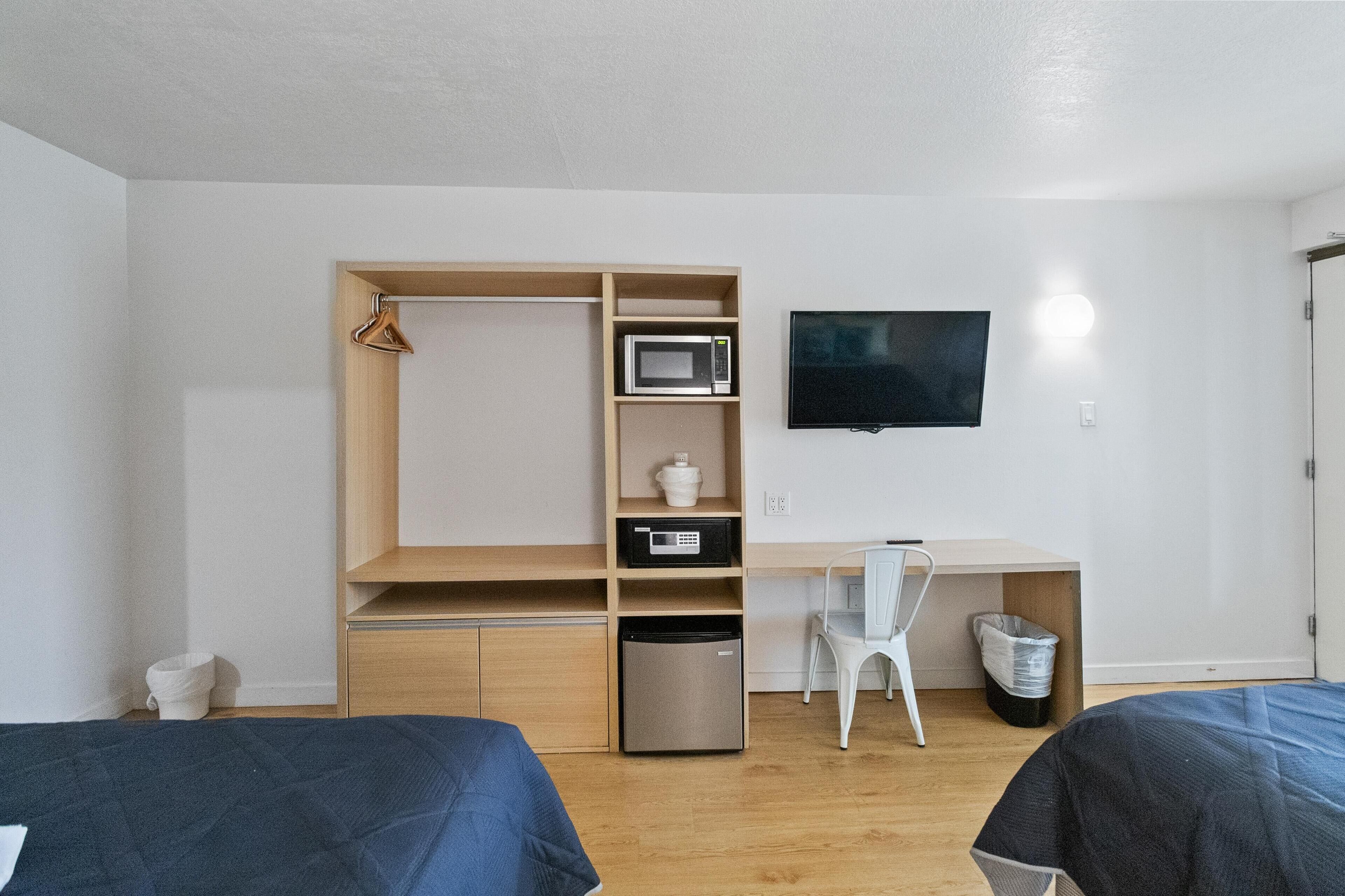 A compact bedroom with a bed, a desk, a chair, a TV, and a small fridge.