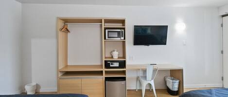 A compact bedroom with a bed, a desk, a chair, a TV, and a small fridge.