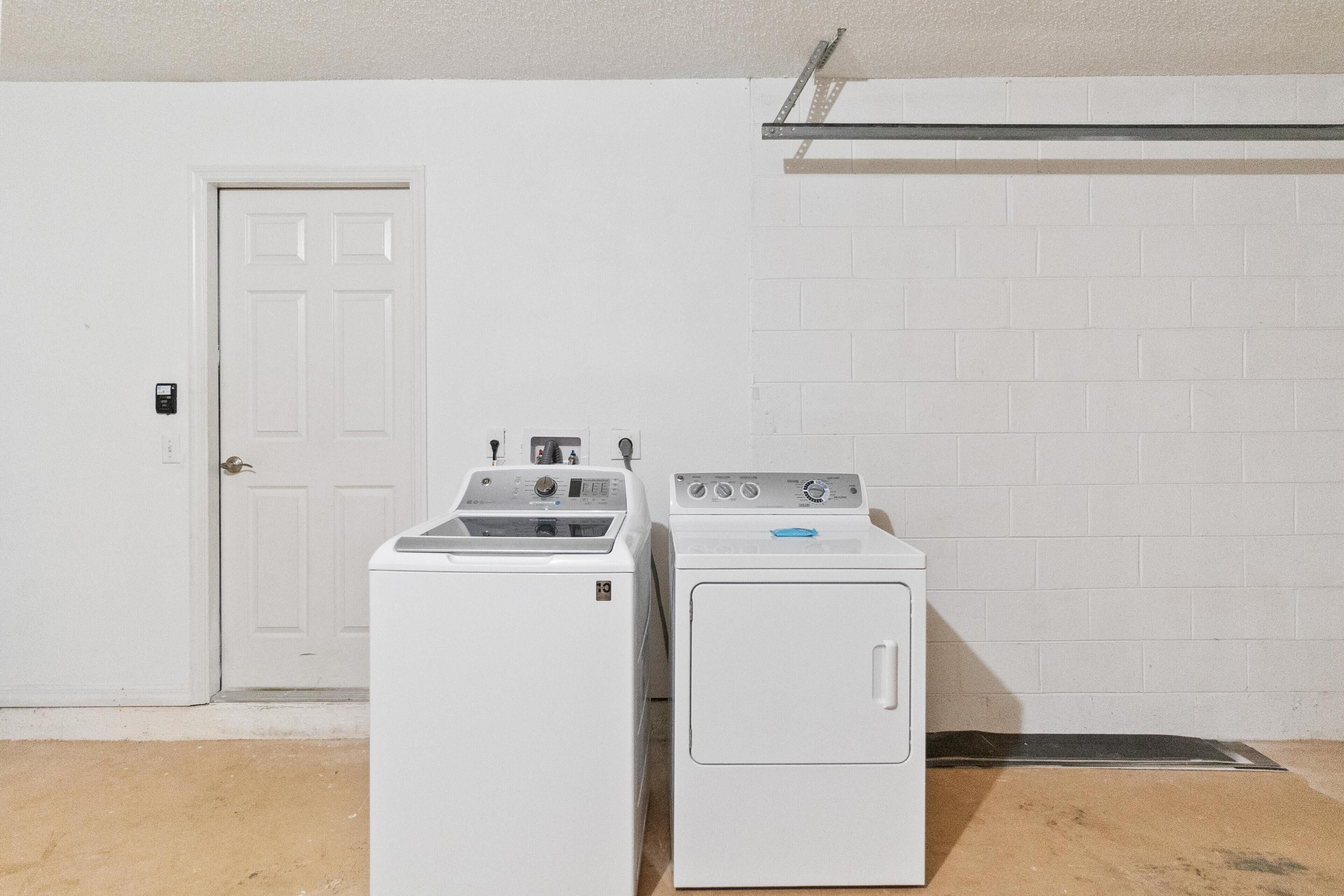 Une buanderie avec deux machines à laver blanches, une porte blanche et un mur en briques blanches.