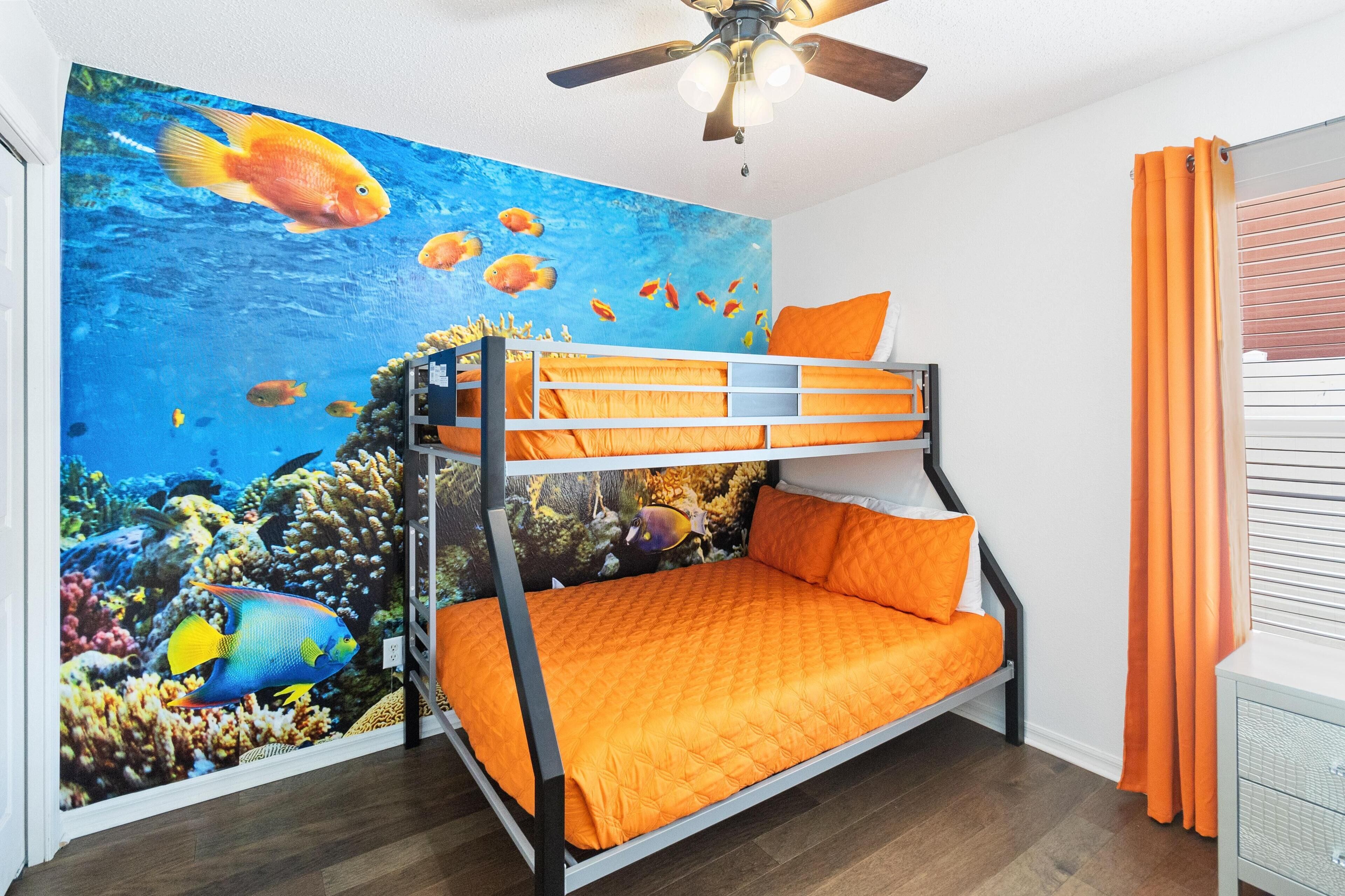 A bunk bed with orange bedding, a ceiling fan, and an ocean-themed mural on the wall.